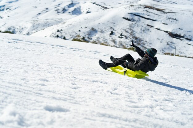 Junger kaukasischer Junge, der mit einem Schlitten auf dem Berg spielt, der mit Schnee bedeckt ist