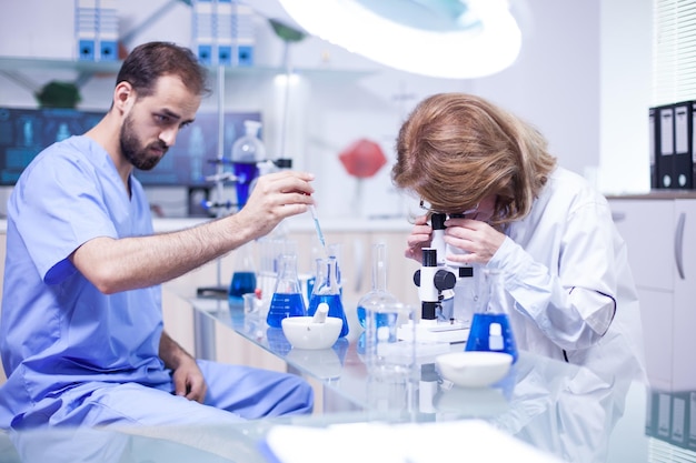 Junger kaukasischer männlicher wissenschaftler, der eine pipette verwendet, analysiert eine flüssigkeit, um moleküle im reagenzglas zu extrahieren. wissenschaftlerin justiert mikroskop.