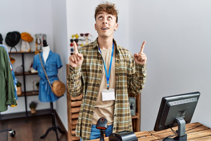 Kostenlose Foto junger kaukasischer mann, der als manager in einer einzelhandelsboutique arbeitet, blickte erstaunt und überrascht auf und zeigte mit fingern und erhobenen armen