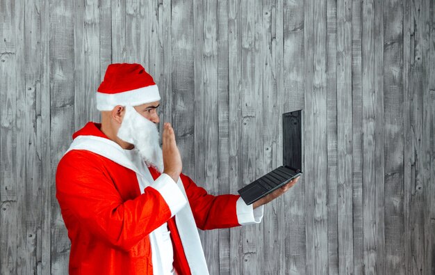 Junger kaukasischer mann, der als weihnachtsmann verkleidet ist und in einem videoanruf auf dem computer winkt.