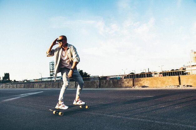 Junger kaukasischer Mann, der auf Longboard oder Skateboard reitet, moderner Schuss im Filmkörnungseffekt und im Weinlesestil.