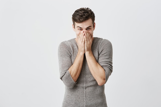 Junger kaukasischer Mann, der Augen abgehört hat, bedeckt Mundblicke in Schrecken, emotional oder ängstlich, nachdem er schockierende Nachrichten im Radio gehört hat, isoliert. Negative Emotionen