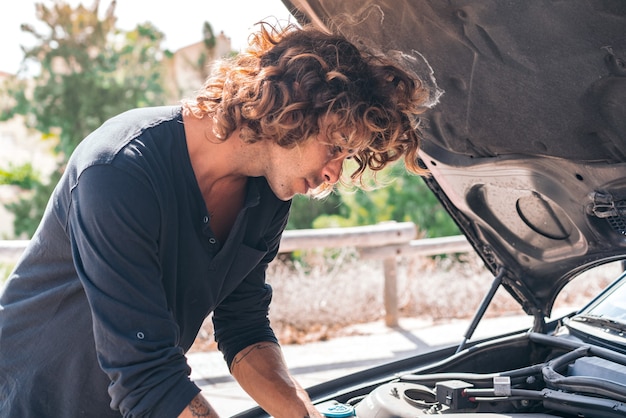 Junger kaukasischer mann, der versucht, ein auto zu reparieren