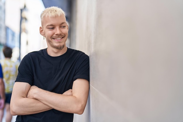 Kostenloses Foto junger kaukasischer mann lächelt selbstbewusst und steht mit verschränkten armen auf der straße