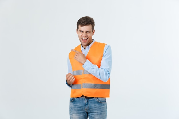 Junger kaukasischer Mann über weißem Hintergrund, der Auftragnehmeruniform und Schutzhelm trägt, überrascht mit einer Idee oder Frage, die mit dem Finger mit glücklichem Gesicht, Nummer eins zeigt.