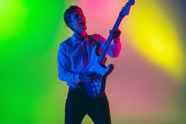 Junger kaukasischer Musiker, Gitarrist, der auf Gradientenraum im Neonlicht spielt. Konzept von Musik, Hobby, Festival