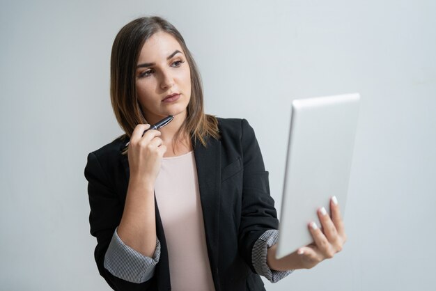 Junger kaukasischer weiblicher Manager, der Tablette hält und Kinn berührt