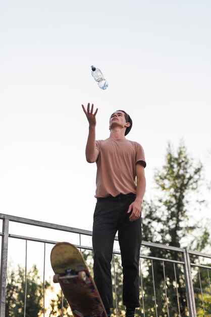 Junger Kerl, der mit Skateboard und Flasche Wasser aufwirft