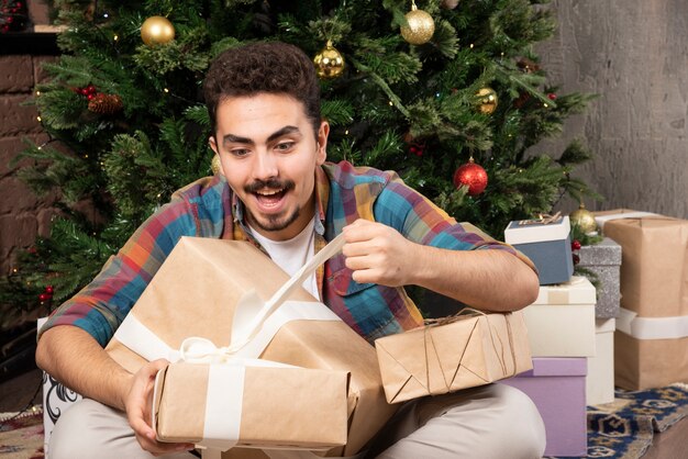 Junger Kerl des Weihnachtsmorgens, der sein Geschenk öffnet.