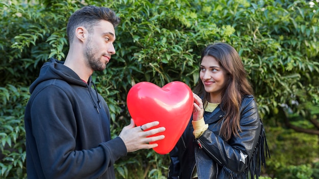 Junger Kerl und lächelnde Dame mit Ballon in der Form des Herzens