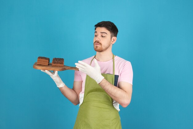 Junger Koch, der frische Schokoladenkuchenscheiben hält.