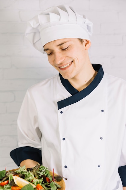 Kostenloses Foto junger koch, der hölzerne platte mit salat hält