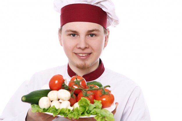 Junger Koch, der Teller mit Gemüse hält