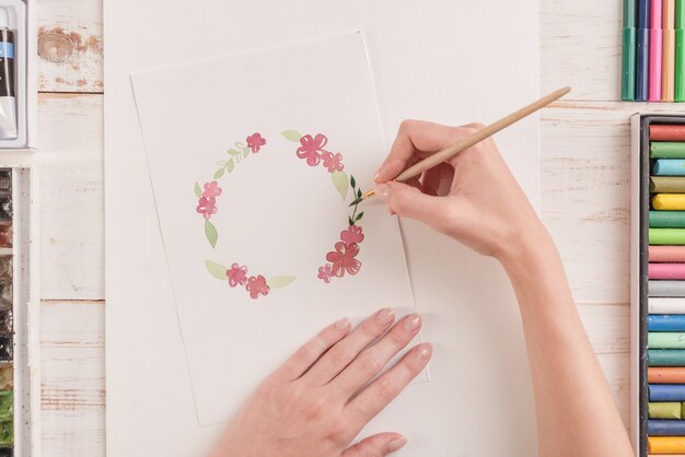 Junger Künstler, der Blumenmuster mit Aquarellfarbe und Pinsel am Arbeitsplatz zeichnet