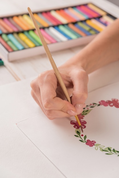 Junger Künstler, der Blumenmuster mit Aquarellfarbe und Pinsel am Arbeitsplatz zeichnet