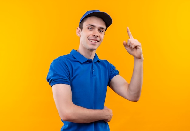 Junger Kurier, der blaue Uniform und blaue Kappe trägt, die glücklichen Zeigefinger oben tut