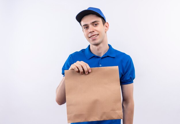 Junger Kurier, der blaue Uniform und blaue Kappe trägt, hält glücklich eine Tasche