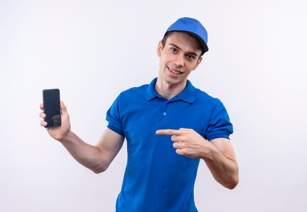 Junger Kurier, der blaue Uniform und blaue Kappe trägt, zeigt glücklich auf das Telefon