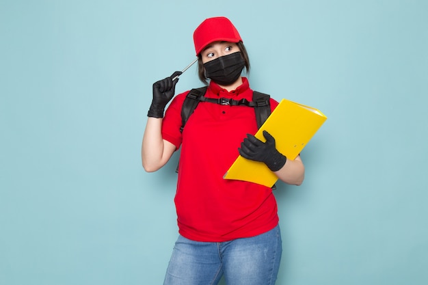 Kostenloses Foto junger kurier in roter polo-roter kappe schwarze sterile schutzmaske schwarzer rucksack, der paket auf blau hält