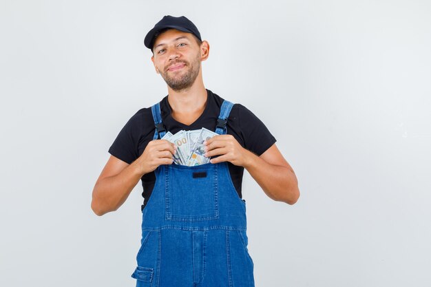 Junger lader, der geld in uniform in seine tasche steckt und fröhlich aussieht, vorderansicht.