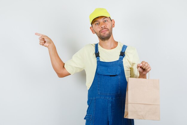 Junger lader, der papiertüte hält und zur seite in der einheitlichen vorderansicht zeigt.