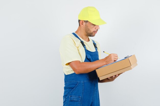 Junger Lader in der Uniform, die Notizen auf Zwischenablage macht und beschäftigt, Vorderansicht schaut.