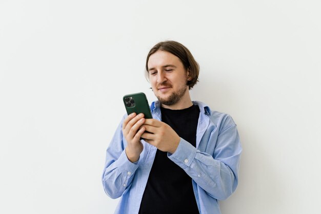 Junger lächelnder Geschäftsmann, der etwas auf dem Handy lokalisiert auf weißem Hintergrund aufpasst Studio-Shooting Kopieren Sie Platz