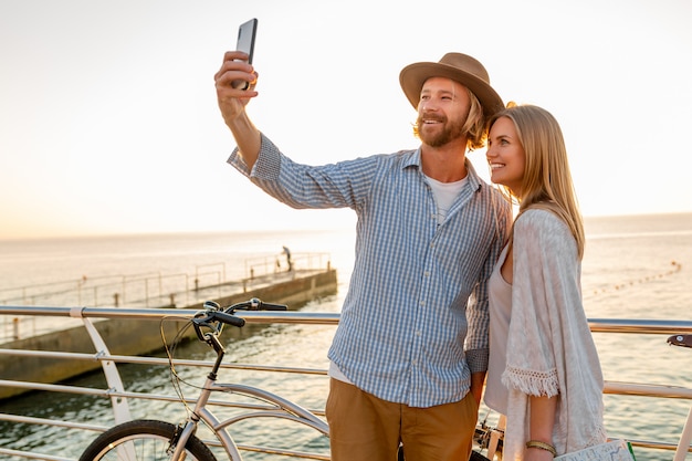 Junger lächelnder glücklicher mann und frau, die auf fahrrädern reisen, die selfie-foto auf telefonkamera machen