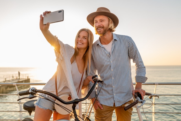 Junger lächelnder glücklicher Mann und Frau, die auf Fahrrädern reisen, die Selfie-Foto auf Telefonkamera machen