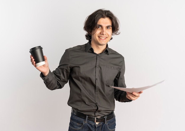Junger lächelnder hübscher kaukasischer Mann hält Kaffeetasse und leere weiße Papierblätter lokalisiert auf weißem Hintergrund mit Kopienraum