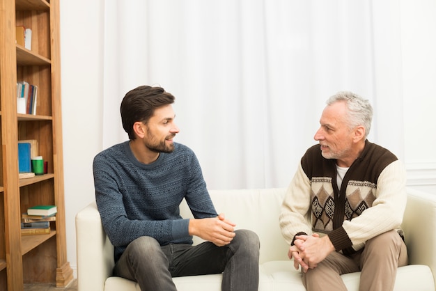 Junger lächelnder Kerl und gealterter Mann, der auf Sofa sitzt