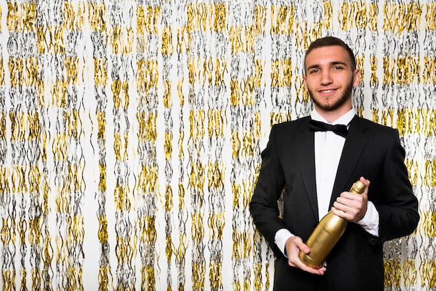 Kostenloses Foto junger lächelnder mann in der abendessenjacke mit flasche des getränks