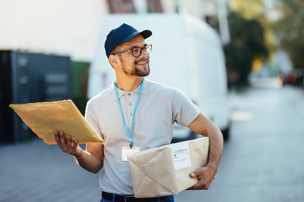 Junger lächelnder Postangestellter, der während einer Lieferung durch ein Wohnviertel geht