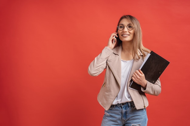 Junger lächelnder Student oder Praktikant in Brillen, die am Telefon sprechen, während sie mit einem Ordner stehen