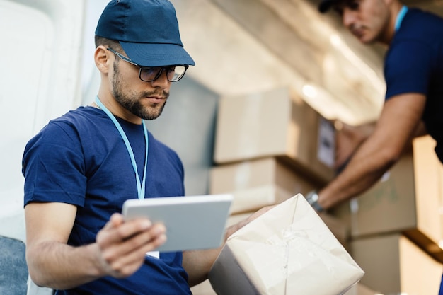 Junger Lieferbote mit Touchpad beim Lesen des Etiketts auf einem Paket