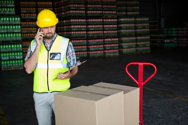 Junger männlicher Arbeiter, der am Telefon in der Fabrik spricht