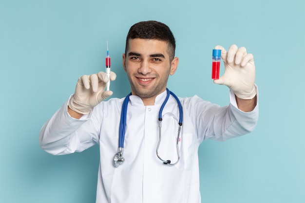 Junger männlicher Arzt im weißen Anzug mit blauem Stethoskop, das Injektion mit smileman männlich hält