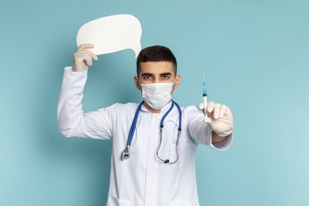 Junger männlicher Arzt im weißen Anzug mit blauem Stethoskop, das Injektion und weißen Schilderjob hält