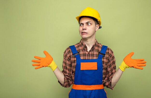 Junger männlicher Baumeister, der Uniform mit Handschuhen trägt, isoliert auf olivgrüner Wand mit Kopierraum