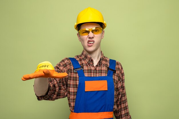 Junger männlicher Baumeister in Uniform und Handschuhen mit Brille isoliert auf olivgrüner Wand