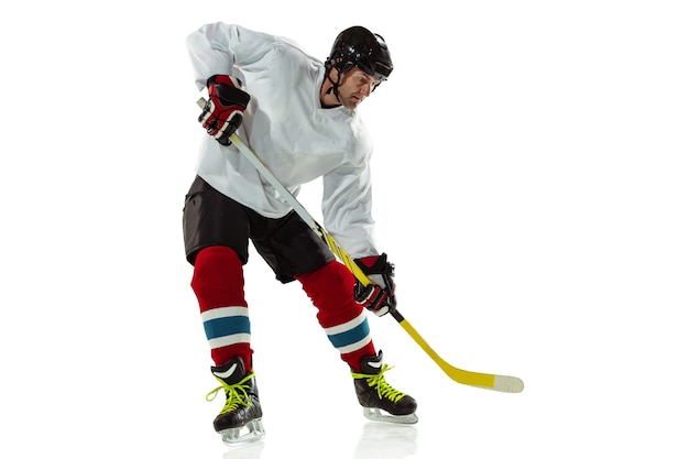 Junger männlicher Hockeyspieler mit dem Stock auf Eisplatz und weißer Wand. Sportler tragen Ausrüstung und Helm üben