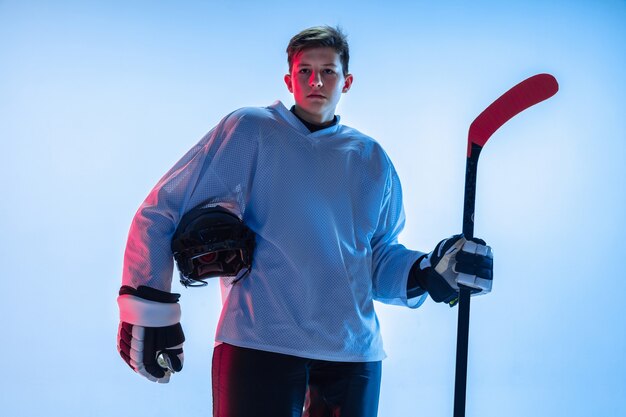 Junger männlicher Hockeyspieler mit dem Stock auf weißer Wand im Neonlicht