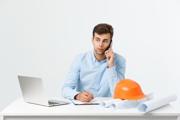 Junger männlicher Ingenieur, der in seinem Büro auf Grau telefoniert.