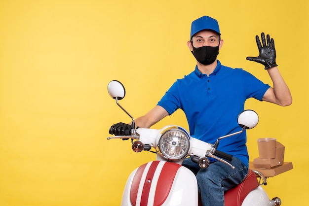 Junger männlicher Kurier der Vorderansicht in der blauen Uniform und in der Maske auf gelbem Hintergrund