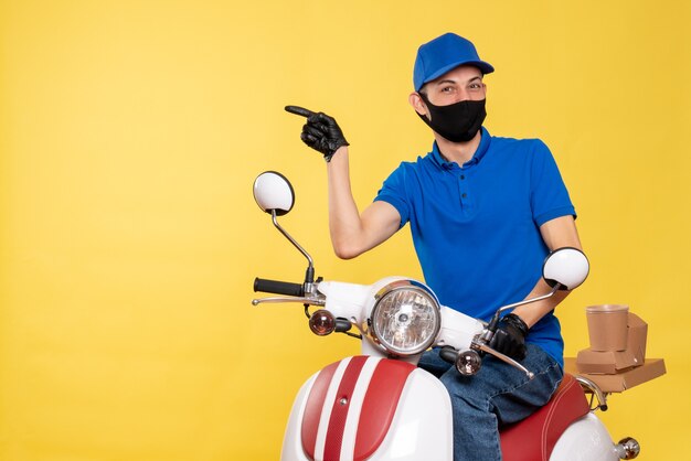 Junger männlicher Kurier der Vorderansicht in der blauen Uniform und in der Maske auf gelbem Hintergrund