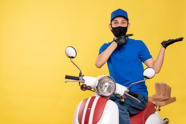 Junger männlicher Kurier der Vorderansicht in der blauen Uniform und in der Maske auf gelbem Hintergrund