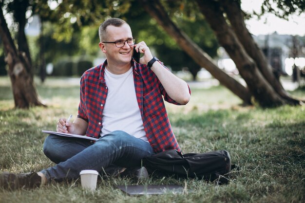 Junger männlicher Student, der an einem Computer im Park arbeitet