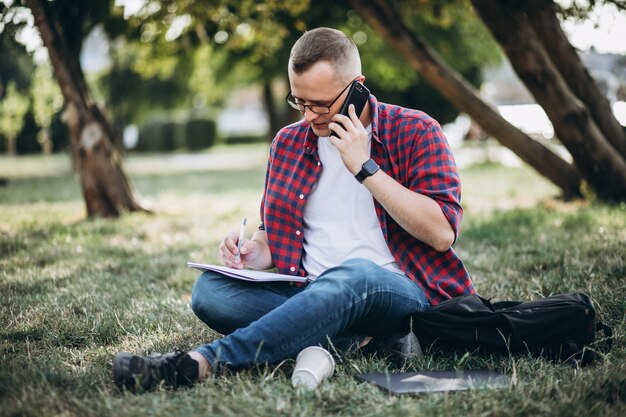 Junger männlicher Student, der an einem Computer im Park arbeitet