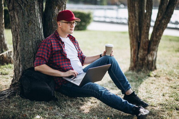 Junger männlicher Student, der an einem Computer im Park arbeitet