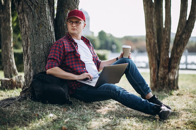 Junger männlicher Student, der an einem Computer im Park arbeitet